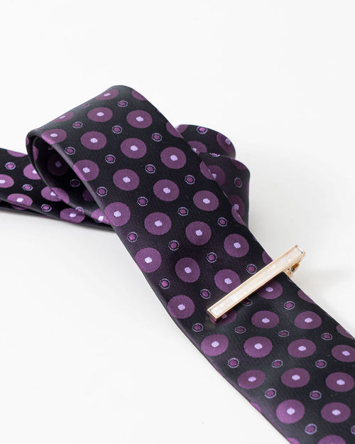 Gold-tone tie clip styled with a black and purple patterned tie